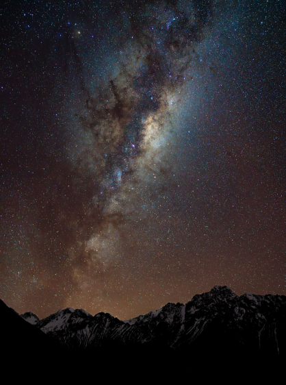 Stargazing in Aoraki Mount Cook, a star filled night sky with the Milky Way over snowy mountains .