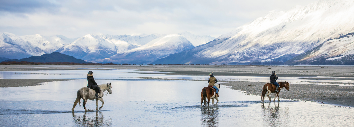 Three travellers explore the stunning landscapes of Glenorchy, Queenstown, on horseback. Their private tour is surrounded by snowcapped mountains.